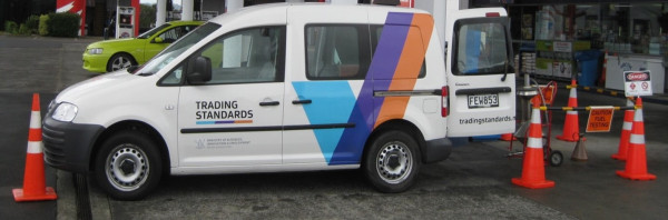 A van with Trading Standards branding parked up with its back doors opened up to an area of traffic cones and a sign reading, Caution fuel testing.